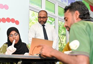 ބިދޭސީންގެ ފިންގަޕްރިންޓާއި ފޮޓޯ ނެގުމުގެ ގައުމީ ކެމްޕެއިން، "ކުރަނގި" ފެށުމަށްފަހު، ބިދޭސީއަކު ފިންގަޕްރިންޓު ޖަހާއިރު ހޯމް ލޭންޑު ސެކިއުރިޓީ މިނިސްޓަރު އިހުސާން މަޑުކޮށްލައްވައިގެން.-- ފޮޓޯ: ނިޝާން އަލީ/ މިހާރު